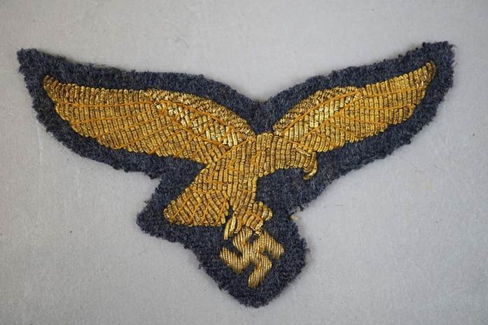 A gold eagle patch on a grey background

Description automatically generated